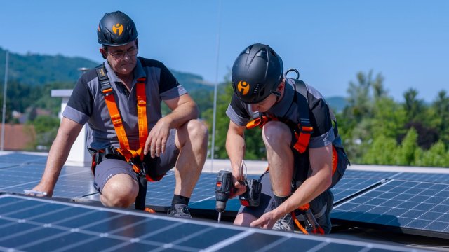 Zwei Monteure verschrauben Photovoltaik-Module auf einem Hausdach.